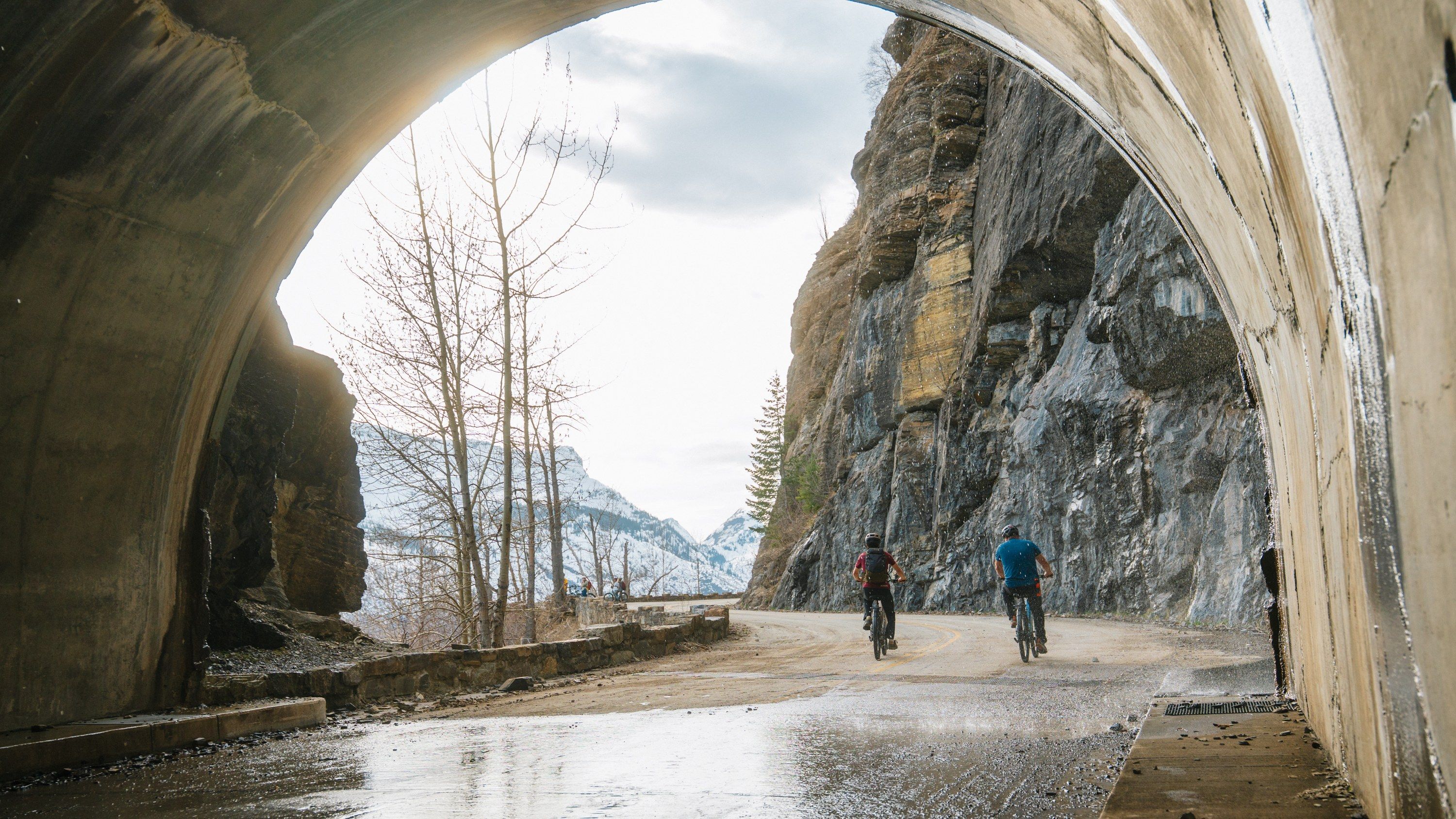 Aventon e-bikes lined up along a stone wall with the mountains of Glacier National Park behind