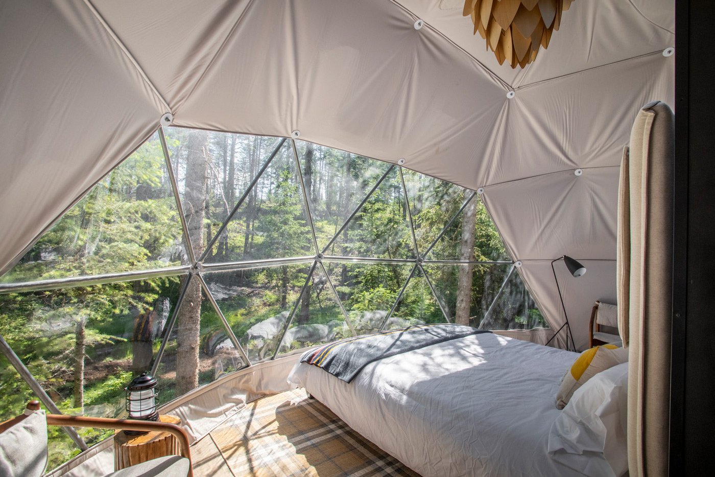 Inside a geodesic dome at BaseGlamp with a bed and a forest view